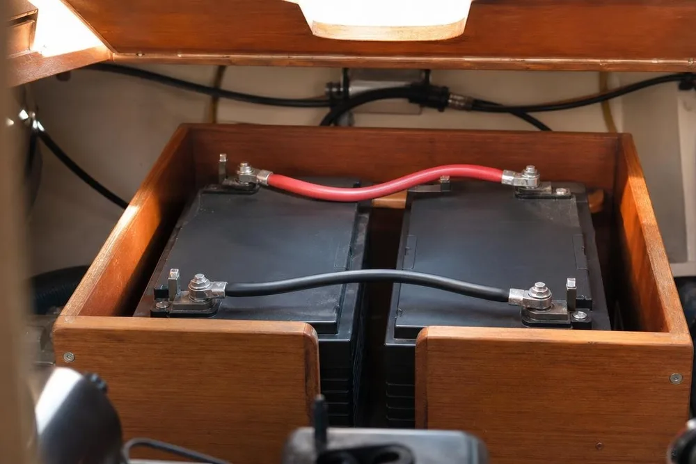 Zwei Batterien nebeneinander im Holzkasten an Bord, oben mit einem roten und unten mit einem schwarzen Kabel verbunden