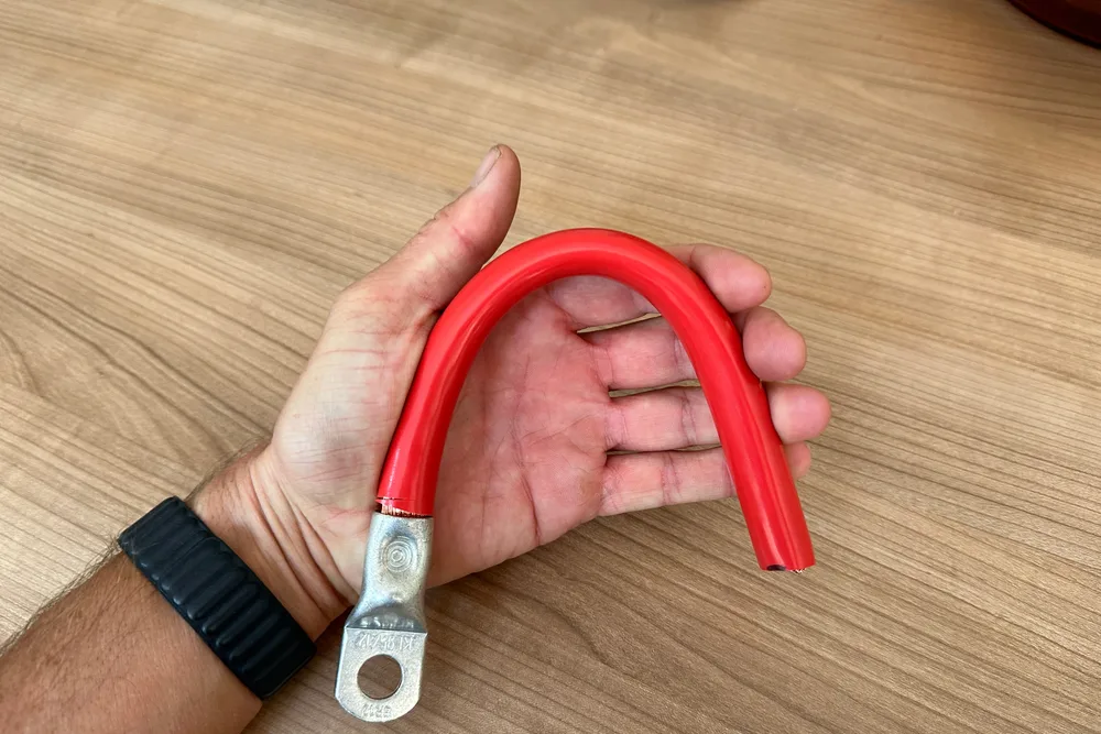 Eine Hand biegt ein rotes Batteriekabel mit Rohrkabelschuh zu einem engen Bogen