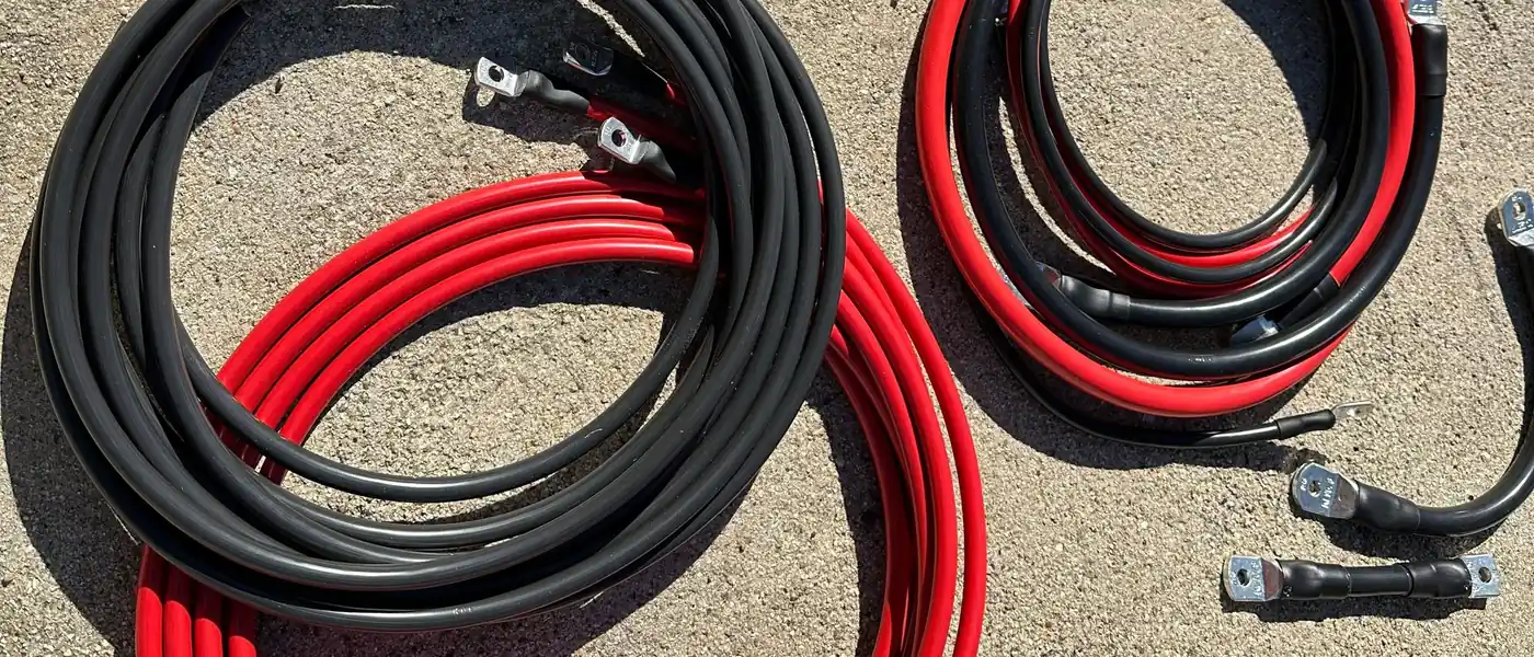 Mehrere fertig konfektionierte rote und schwarze Batteriekabel mit
         Rohrkabelschuhen und Schrumpfschlauch, aufgerollt auf einem Steinboden in der Sonne