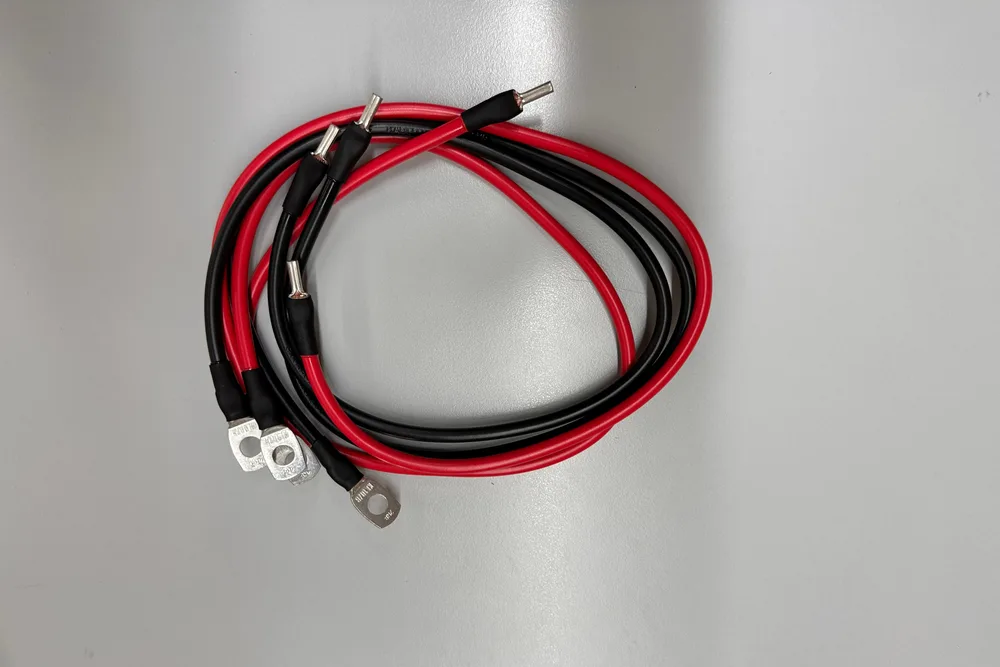 Ein rotes und ein schwarzes Batteriekabel gleicher Länge, aufgerollt, mit Rohrkabelschuhen an den Enden