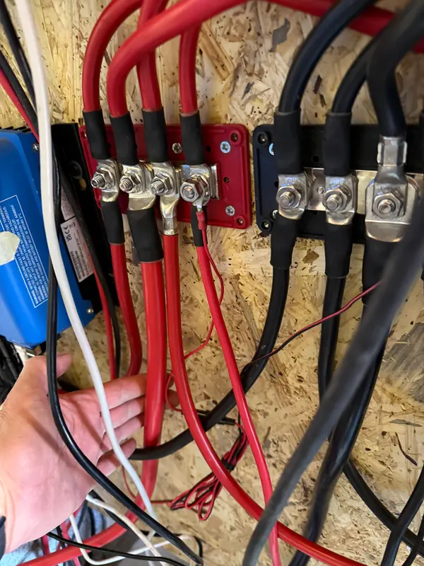 Rote und schwarze Batteriekabel mit Rohrkabelschuhen an zwei Sammelschienen
         für Plus und Minus auf einer Holzwand