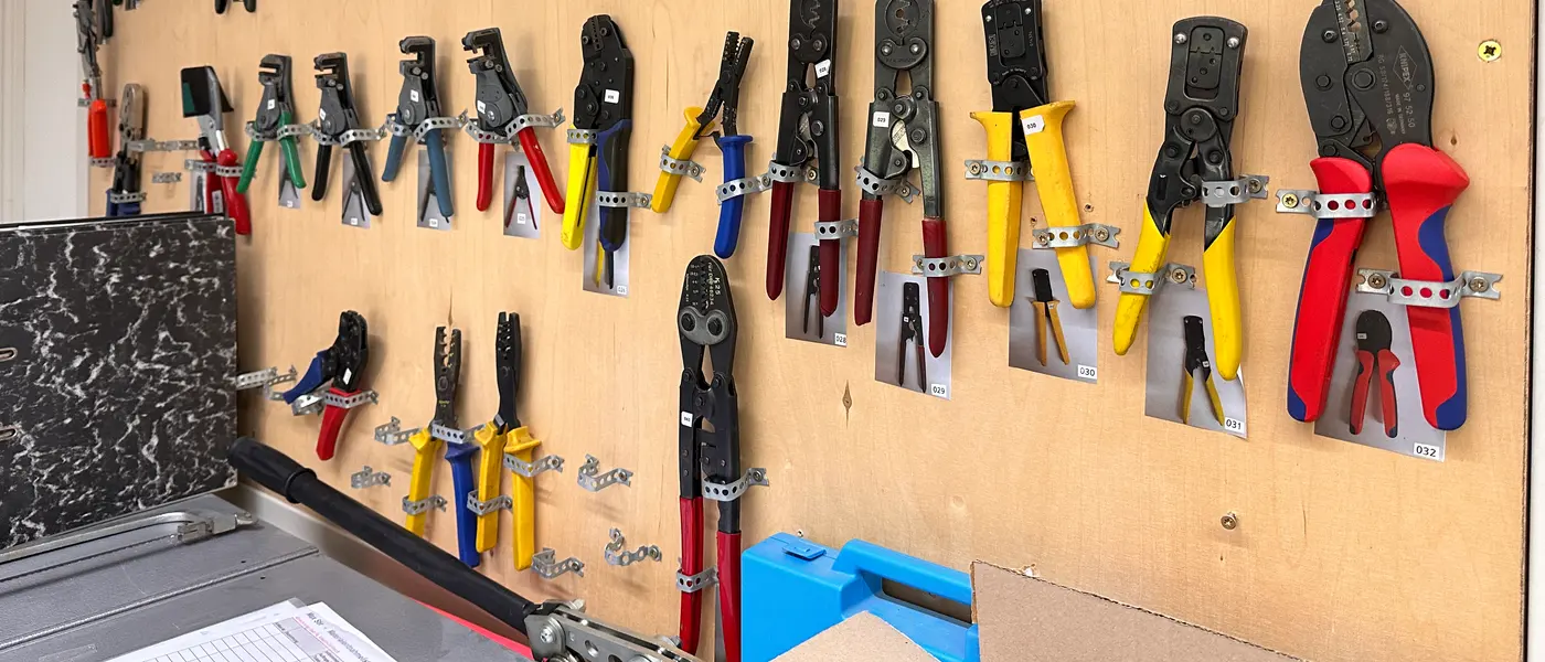Workshop wall with around twenty crimping and stripping tools of
         different sizes hanging on it