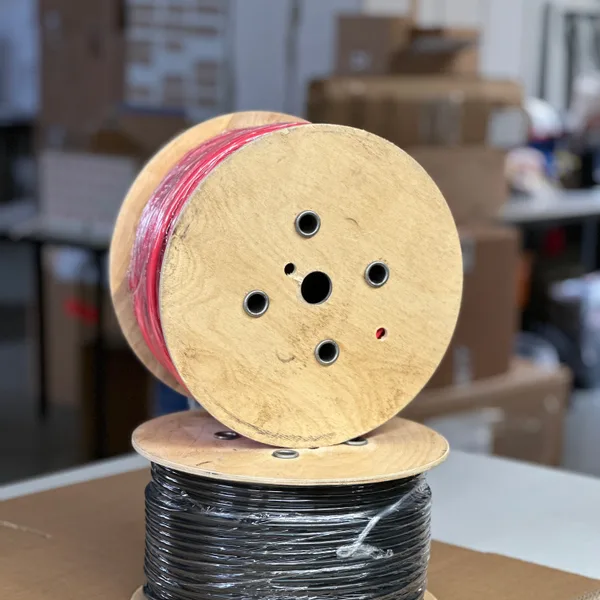 Holztrommel mit roter Fahrzeugleitung, aufgestellt auf einer Trommel mit schwarzer Leitung