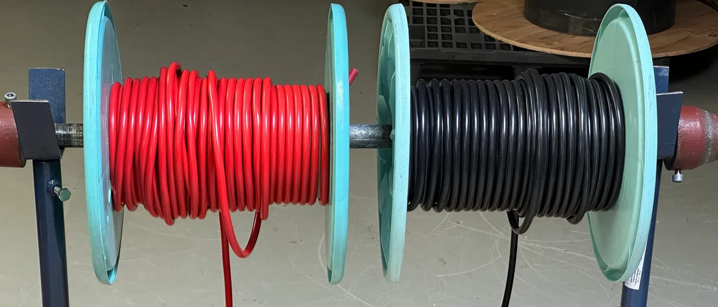 Zwei große Kabeltrommeln mit rotem und schwarzem Batteriekabel auf
         Abrollböcken in der Fertigung