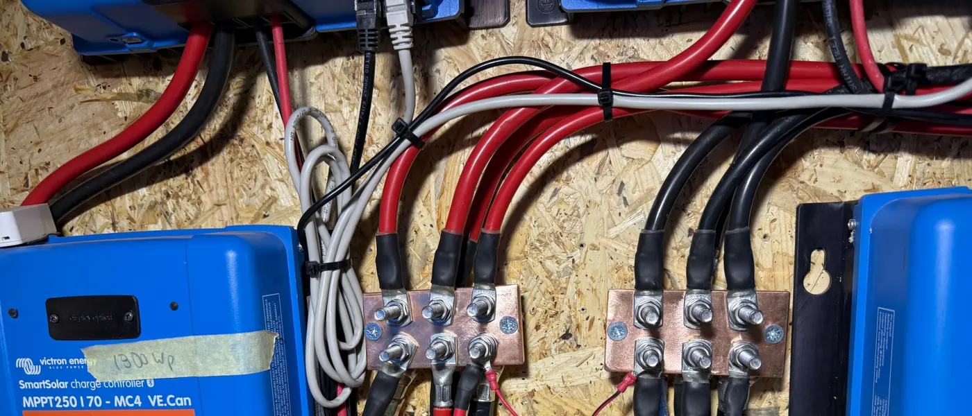 Solarladeregler an einer Holzwand, daneben zwei Sammelschienen aus Kupfer mit roten und schwarzen Leitungen und Rohrkabelschuhen