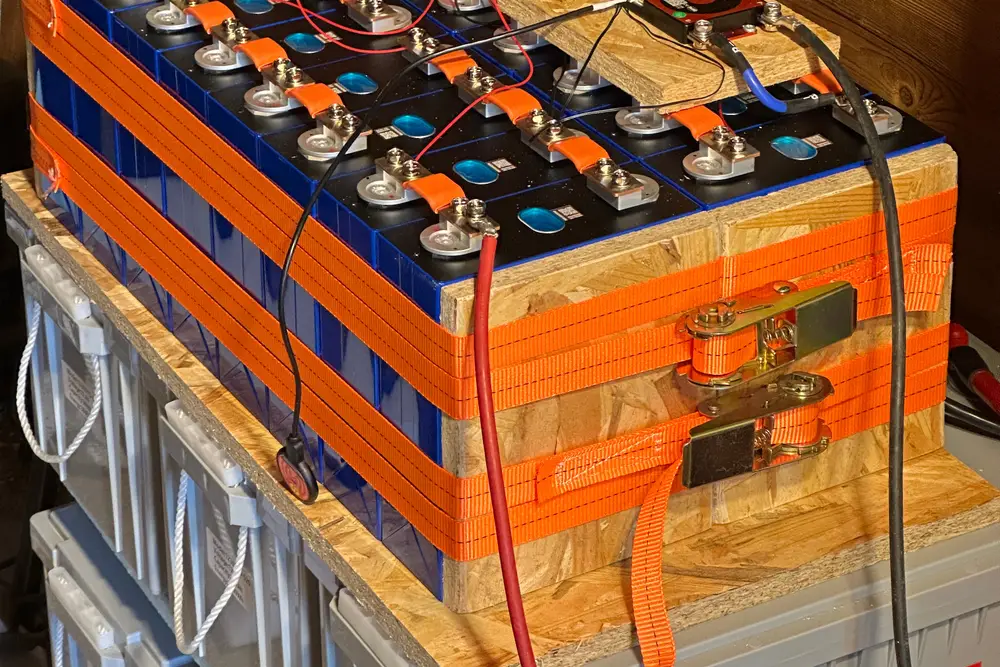 Selbstgebauter LiFePO4-Block aus blauen Zellen mit orangen Spanngurten, orange isolierten Zellverbindern und den Messleitungen des Batteriemanagements