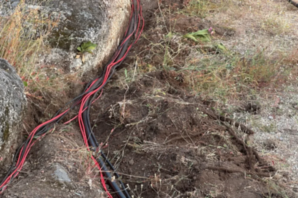 Rotes und schwarzes Solarkabel, offen über Fels und trockenen Boden zu einer Anlage verlegt