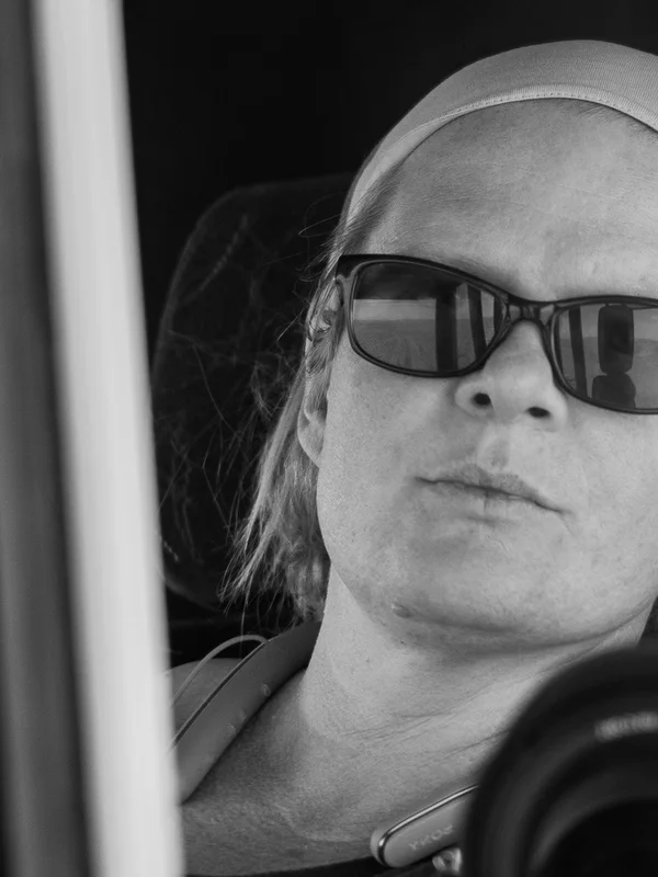 Black-and-white portrait of Tanja Moosmann wearing sunglasses and a
         headband, taken inside a vehicle